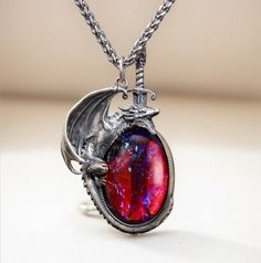 Embrace your inner strength and mythical allure with this stunning handcrafted dragon necklace. The dragon, made of 925 sterling silver, wraps protectively around a mesmerizing "Dragon's Breath" stone, which shimmers with an otherworldly mix of fiery reds and deep purples, reminiscent of mystical flames. The intricate detailing of the silver dragon captures its fierce yet elegant nature, and the sword behind the dragon adds an element of bravery and protection. The necklace hangs from a durable titanium chain, ensuring lasting quality and comfort.  This unique piece is perfect for fantasy lovers, dragon lover, or anyone looking to add a touch of magic to their jewelry collection. Material: Pendant: Sterling silver(dragon), dragon breath glass Chain: 22 inches titanium Silver Dragon Necklace, Dragon Bracelet, Jewelry Purple, Dragon Lover, Dragon Necklace, Magical Jewelry, Crystal Opal, Silver Dragon, Dragon Pendant