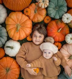 two young children standing next to each other surrounded by pumpkins