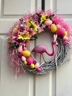 a pink flamingo wreath with easter eggs and flowers hanging on the front door,