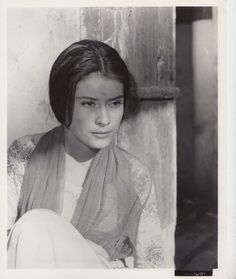 an old black and white photo of a young woman wearing a shawl sitting in front of a door