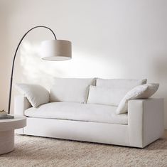 a white couch sitting on top of a living room floor next to a tall lamp