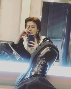 a woman sitting on a couch looking at her cell phone while wearing black leather boots