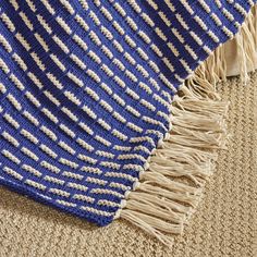 a blue and white blanket laying on top of a carpet next to a rug with fringes