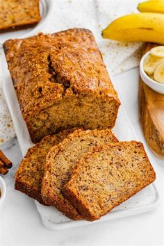 sliced loaf of banana bread on a white plate with cinnamon and bananas in the background