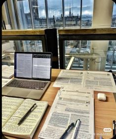 an open laptop computer sitting on top of a wooden table next to papers and pen