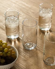 three glasses and one bowl filled with grapes on a wooden table next to each other