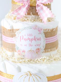 a three tiered cake decorated with pink and gold ribbon, pumpkin sign on top