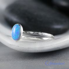 This Sterling Silver Blue Opal Ring features an 8 mm x 6 mm oval lab grown Blue Opal cabochon that has been securely set in a highly polished fine silver bezel. The band is made of a sturdy round Sterling Silver wire that has a hammered texture around the entire band. These beautiful rings make unique promise rings, lovely stacking rings, great birthstone rings, or just a wonderful love tokens for yourself or your special someone. This man-made Blue Opal is created from very uniform nanoparticle Classic Blue Oval Opal Ring, Modern Oval Cabochon Opal Ring As Gift, Classic Blue Opal Ring As A Gift, Classic Blue Opal Ring As Gift, Classic Blue Opal Ring For Gift, Classic Blue Opal Ring Gift, Stackable Oval Opal Rings, Classic Blue Opal Round Ring, Classic Oval Blue Moonstone Ring