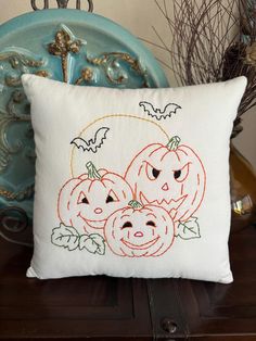 a white pillow with three pumpkins on it sitting on top of a table next to a blue chair