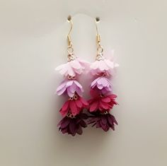 two pairs of pink and purple flowers hanging from gold earwires on a white surface