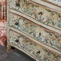 an ornate painted chest of drawers next to a brick wall