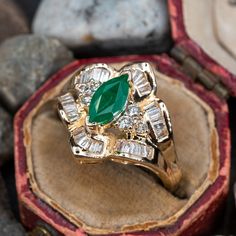 This elegant ring is centered with one (1) marquise cut natural emerald set into a two-prong setting. The emerald is bordered with six (6), prong set, round brilliant cut diamonds and thirty (30), channel set, baguette cut diamonds. The ring measures 16.0mm at the top, rises 7.8mm above the finger, tapering to 2.0mm wide and 1.1mm thick at the base of the shank. This ring is currently a size 6.75. There is a faint surface line inclusion on the emerald. Luxury Yellow Gold Emerald Ring Marquise Cut, Luxury Yellow Gold Emerald Ring With Intricate Design, Green Marquise Emerald Rings, Marquise Emerald Diamond Ring In Green, Green Marquise Emerald Diamond Ring, Fine Jewelry Marquise Cut Diamond Emerald Ring, Fine Jewelry Diamond Emerald Ring Marquise Cut, Emerald Diamond Ring For May Birthstone In Marquise Shape, Green Marquise Diamond Ring For Formal Occasions