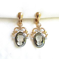 This timeless glass cameo pair is not signed and is probably from the 1970's costume jewelry era.  Each earring face measures 1 5/8" tall by 7/8" wide and features a raised frosted white glass cameo, set atop an oval shaped black glass base.  Five round cut opal glass rhinestones sparkle at the top of each cameo.  Each cameo is glue set with an enclosed backside.  The clip back fixtures are working properly with secure hold when worn.  There are no hallmarks and this pair is in very good vintage condition.    Comes carefully gift boxed for safe and secure delivery. I also ship daily, everyday, except on Sundays, so your parcel may be on its way to you today.  Shipping upgrades are available, i.e. priority and express via USPS international and domestic post.  All of my items listed are VIN Luxury Oval Cameo Earrings, 1970s Costume, Luxury Vintage Oval Clip-on Earrings, Vintage Black Round Clip-on Earrings, Promo Coupon, Vintage Yellow Gold Clip-on Earrings With Cabochon, Vintage Gold Clip-on Earrings With Black Enamel, Vintage Clip, Black Glass