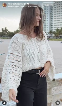 a woman standing on top of a wooden deck next to the ocean with her hands in her pockets