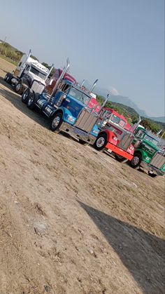 a row of semi trucks parked on top of a dirt field