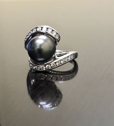 DeKara Designs Collection Beautiful Art Deco/Vintage/Modern Style Pearl Engagement Ring. Metal- 14K White Gold, .583. Stones- 10 MM Round Tahitian/South Sea Black Pearl, 24 Round Diamonds, F-G color SI1-SI2 Clarity, 0.62 Carats. The ring is beautiful with a unique Tahitian pearl that is round in shape. This is a fantastic pearl that is also rare to find. The diamond has two rows of channel set diamonds that are all equivalent in size. The pearl is professionally set in the center of the ring. Si Black Luxury Pearl Ring For Formal Occasions, Classic Black Pearl Ring For Anniversary, Classic Black Pearl Ring For Wedding, Black Pearl Formal Ring With Round Shape, Formal Black Pearl Ring With Round Shape, Classic Black Pearl Ring, Black Pearl Ring In Fine Jewelry Style, Black Pearl Ring Fine Jewelry, Fine Jewelry Black Round Pearl Ring