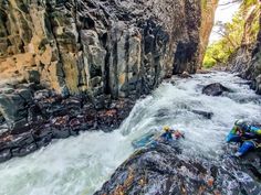 two people in kayaks are paddling through the water near large rocks and cliffs