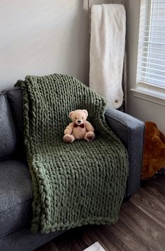 a teddy bear sitting on top of a couch covered in a green knitted blanket