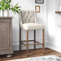 a white bar stool in front of a wooden cabinet and potted plant next to it