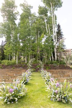 an outdoor ceremony set up with wooden chairs and flowers in the foreground, surrounded by tall trees