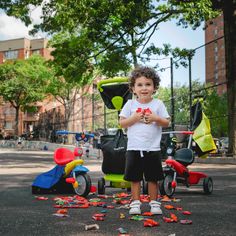 a young boy standing in the middle of a street with toys all around him and on the ground