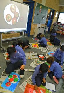 children are sitting on the floor in front of a projector screen and doing arts and crafts