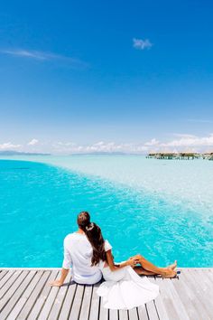 two people sitting on a dock looking out at the water