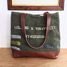 There is all kinds of history behind the WWII era soldier's duffle bag canvas that was used in this carryall tote and it is ready for more adventures.  The front of the reconstructed bag features the original hand painted name and graphics of the soldier that carried the duffle.  The back of the tote was part of a bag that carried WWII era telescopic splints.  Lots of room and will easily carry enough items for a weekend getaway.  Description features: *Authentic WWII era duffle bag canvas with original graphics *Hand cut new quality leather handles of premium chestnut brown leather *Hand hammered solid copper rivets with aged patina *Interior lining: Sturdy 12 oz beige linen canvas with slip pockets for cell phone pens and other items *Leather and chain American Harvest Bag logo tag Throu Vintage Khaki Shoulder Bag For Everyday, Everyday Vintage Khaki Shoulder Bag, Adventure Khaki Bags With Waxed Finish, Khaki Adventure Bags With Waxed Finish, Khaki Adventure Bag With Waxed Finish, Vintage Large Capacity Canvas Shoulder Bag, Canvas Khaki Duffle Bag For Everyday, Khaki Canvas Duffle Bag For Everyday Use, Khaki Canvas Duffle Bag For Daily Use