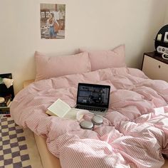 an open laptop computer sitting on top of a pink comforter in a bed room