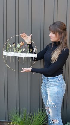 a woman in ripped jeans holding up a wire sculpture with birds on it and plants growing out of it