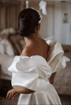 a woman in a white dress is standing near a bed and looking into the distance