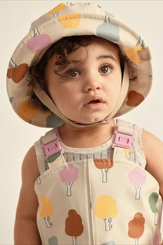 a young child wearing a sun hat with trees on it's brim and suspenders