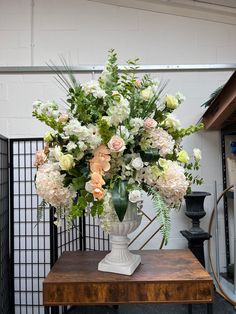 a vase filled with white and pink flowers on top of a wooden table next to a black fence