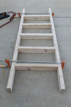 a ladder made out of wood with tools on the ground next to it and some wires