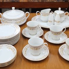 a wooden table topped with lots of white dishes and cups covered in gold trimmings