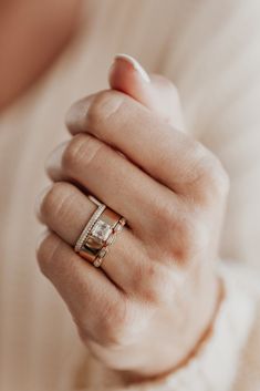 a woman's hand wearing a gold ring with two diamonds on it and a white sweater