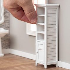 a hand reaching for a white shelf in the corner of a room with wood floors