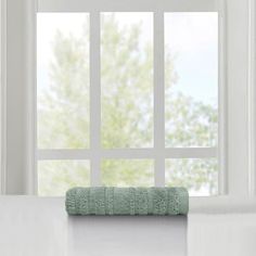 a green towel sitting on top of a white counter next to a window with trees in the background