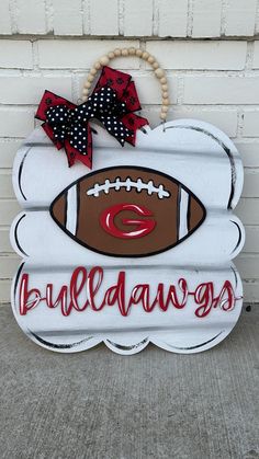 a wooden sign that says bulldogs with a football on it and a bow hanging from the front