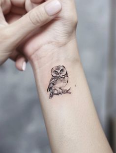 an owl tattoo is on the wrist of a woman's left hand, while she holds her right arm