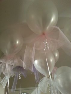 some white balloons are hanging from the ceiling with pink ribbons and bows on them,