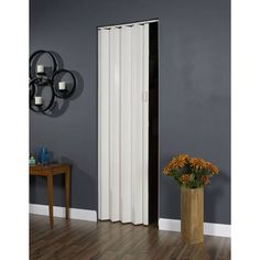 a tall white sliding door next to a vase with flowers on the floor in front of a gray wall