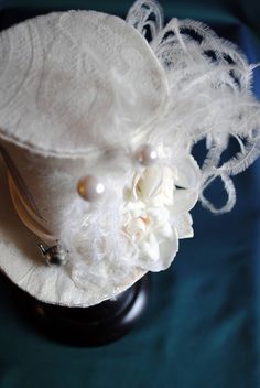 A Mad Hatter fascinator hat with a bridal twist! The hat is covered with beautiful textured ivory brocade and embellished with ivory satin ribbon around the crown. Trimmed with pearl hats pins, ivory roses and hydrangea blossoms,ivory feather spray, the signature 10/6 Mad Hatter card and of course a tiny silver tea-pot! Cause around here it's always tea-time! Both hat pins have push-in clasps to avoid accidents! Veil may be added at an extra cost. This mini top hat is fully lined with satin and Vintage White Costume Hat For Formal Occasions, Vintage White Formal Costume Hat, Elegant White Hat For Gift, Vintage White Mini Hat For Royal Ascot, Cream Short Brim Top Hat For Formal Occasions, White Curved Brim Fascinator For Vintage Events, Elegant White Hat For Vintage Events, Elegant White Hats For Vintage Events, Vintage White Hat With High Crown