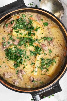 a pot filled with meat and vegetables on top of a stove next to a spoon