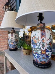 two lamps sitting on top of a table next to a potted plant and lamp shade