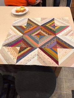 two people standing at a table with a quilted star on it and plates of food in the background