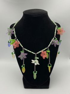 Handcrafted necklace with green and white beads, purple and pink flower charms with leaves adjustable length 17.5-20 inches Green Bohemian Flower Charm Necklace, Handmade Multicolor Fairycore Jewelry, Handmade Whimsical Flower Necklaces, Whimsical Handmade Flower Necklaces, Handmade Green Dangle Crystal Necklace, Adjustable Necklace With Flower Charm, Green Handmade Dangle Crystal Necklaces, Adjustable Dangle Necklace With Flower Charm, Green Flower Necklace With Colorful Beads