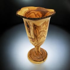 a wooden vase sitting on top of a white table next to a black light background