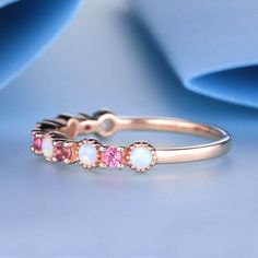 three stone ring with pink and white opal stones on the side, set in rose gold