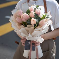 a woman holding a bouquet of pink tulips in her hands on the street